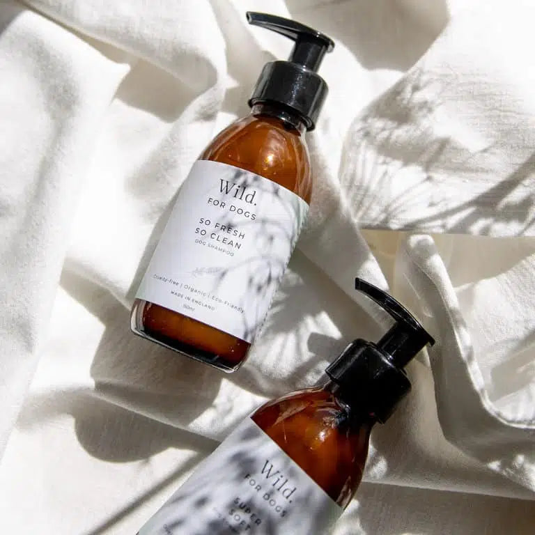 Two Wild For Dogs amber pump bottles of organic shampoo and conditioner on white fabric