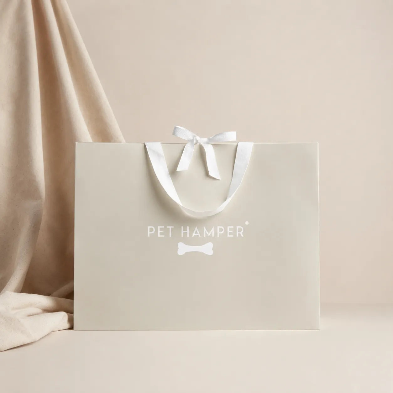 Beige Pet Hamper branded gift bag with white ribbon bow and bone logo