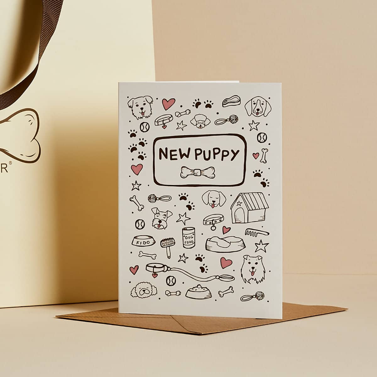 White 'New Puppy' greeting card with illustrated puppy items and doodles, kraft envelope
