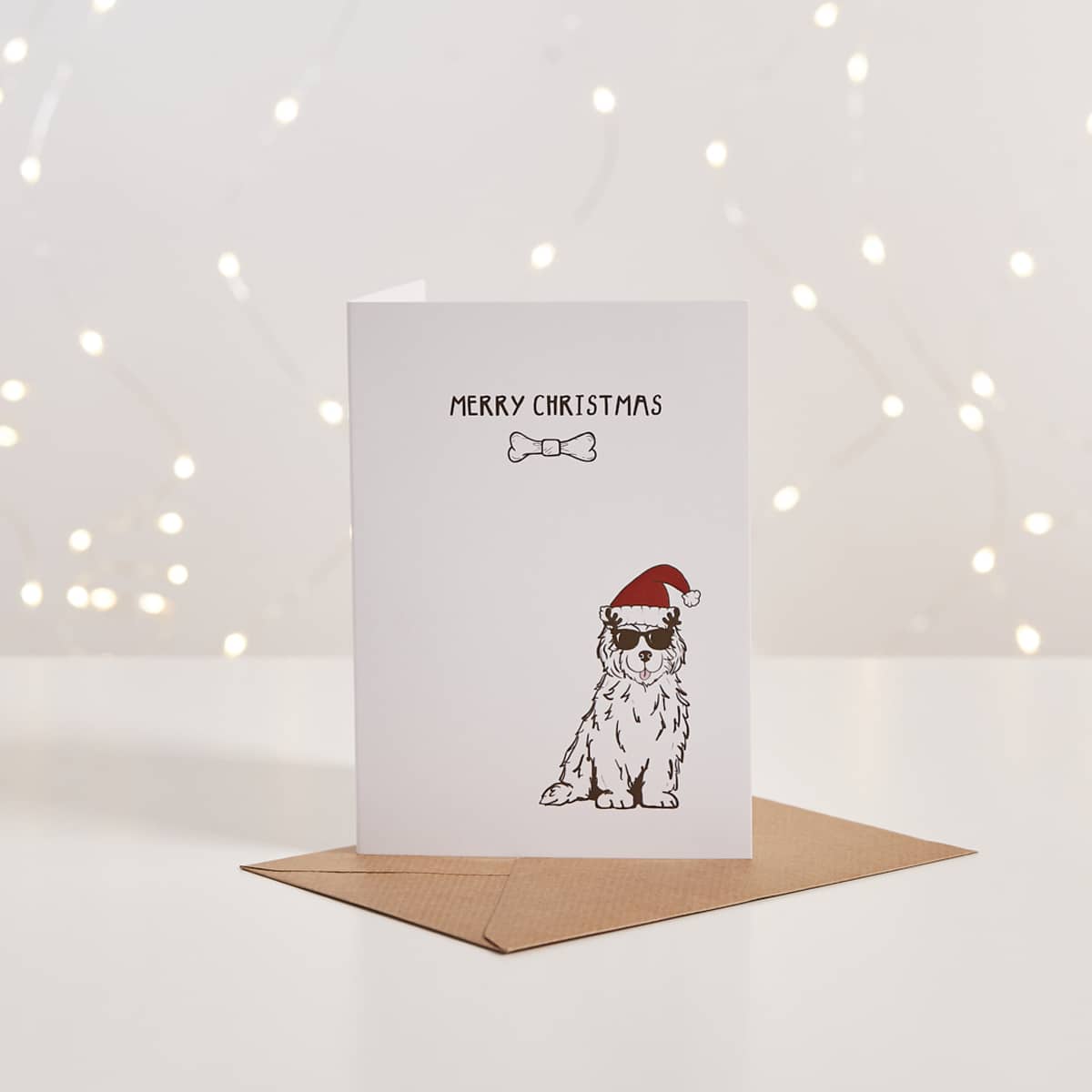 White Christmas card with illustrated dog in Santa hat and sunglasses, 'Merry Christmas' text, kraft envelope