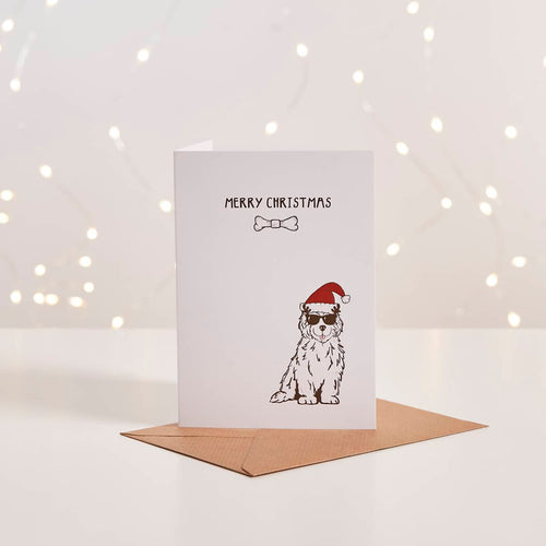 White Christmas card with illustrated dog in Santa hat and sunglasses, 'Merry Christmas' text, kraft envelope