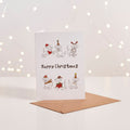 White Christmas card with illustrated puppies wearing festive hats, 'Happy Christmas' text, kraft envelope