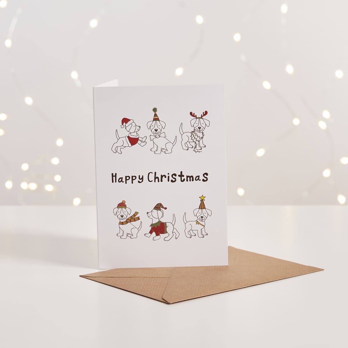 White Christmas card with illustrated puppies wearing festive hats, 'Happy Christmas' text, kraft envelope