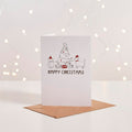 White Christmas card with illustrated cat and dog decorating a tree, 'Happy Christmas' text, kraft envelope