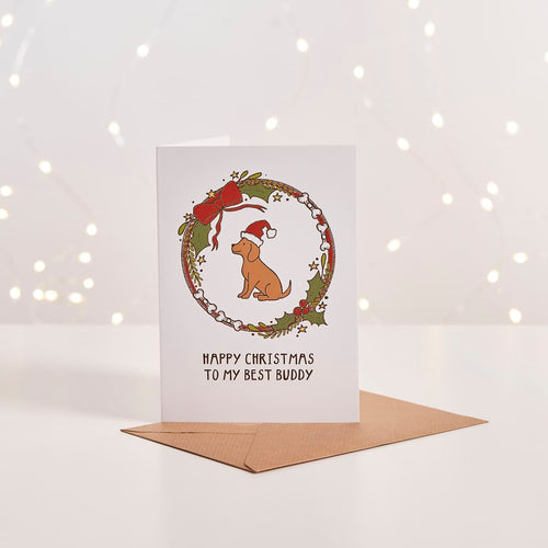 White Christmas card with illustrated dog in Santa hat inside a wreath, 'Happy Christmas to my best buddy' text, kraft envelope