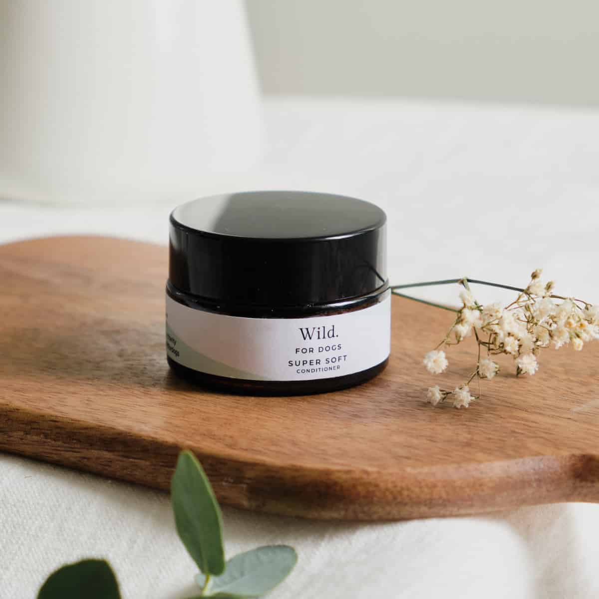 Small dark glass jar of Wild For Dogs Super Soft organic conditioner, travel size, on wooden board