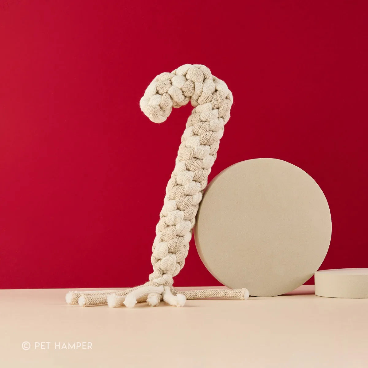 Beige braided rope candy cane dog toy with vanilla scent, red backdrop