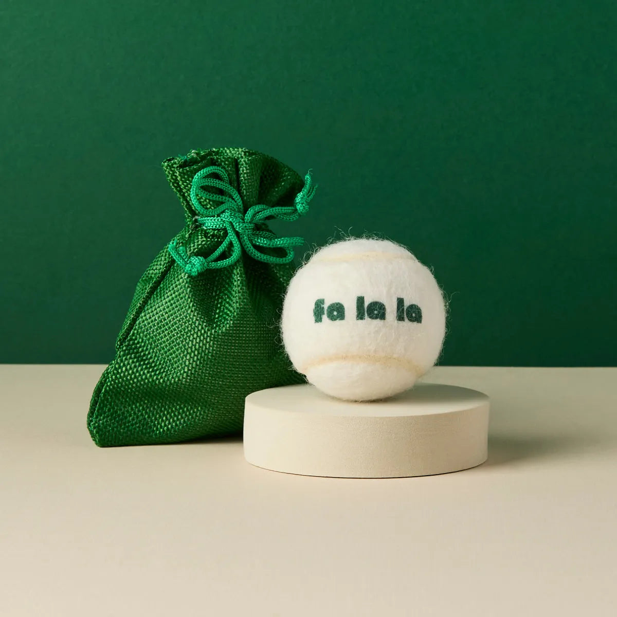 White tennis ball printed with 'Fa La La' text and green gift bag, Pet Hamper